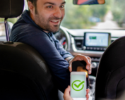 Rideshare driver looking in the back seat of his car and using his phone to verify ride with passenger.